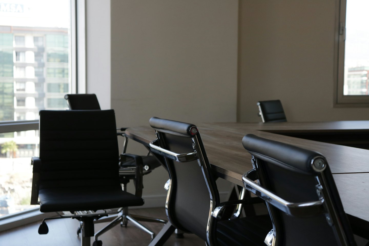 Sala riunioni moderna e vuota con tavolo in legno chiaro e sedie nere.